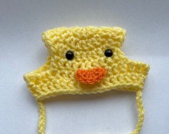 May include: A yellow crocheted baby hat with black eyes, an orange beak, and yellow ties.