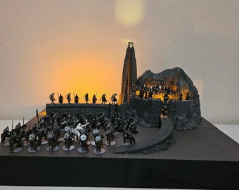 May include: A miniature model of a fantasy castle with a tall tower and a surrounding wall. The castle is made of gray and brown plastic and is set on a black base. There are many small figures of soldiers in front of the castle.