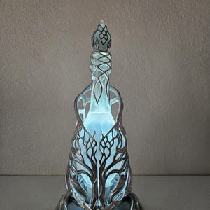 May include: A decorative glass bottle with a silver-coloured metal filigree design. The bottle has a tree-like pattern and a blue glowing interior. The bottle is an artistic piece, suitable for display.