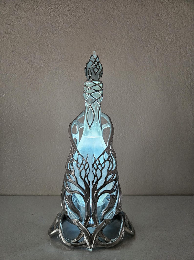 May include: A decorative glass bottle with a silver-coloured metal filigree design. The bottle has a tree-like pattern and a blue glowing interior. The bottle is an artistic piece, suitable for display.