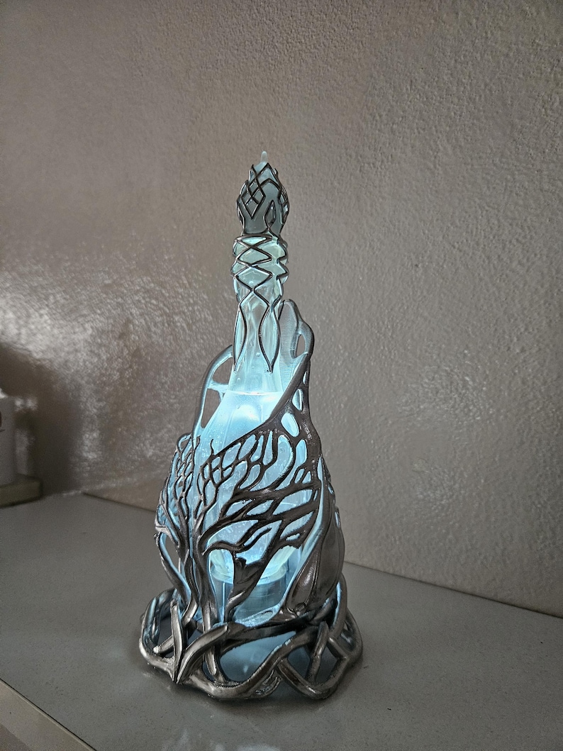 May include: A decorative glass bottle with a silver-coloured, tree-like design. The bottle has a blue interior that glows, and the silver design wraps around the glass. The bottle has a decorative stopper.