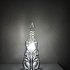 May include: A decorative lamp with a black and white tree design. The lamp has an openwork pattern and a glowing interior. The base and top are also intricately designed. The lamp is lit, creating a soft, ambient glow.