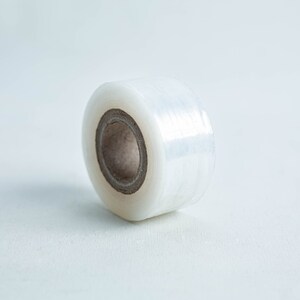 May include: A roll of clear cling film on a white surface. The film is wound around a cardboard core.