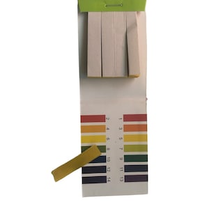 May include: A pack of pH test strips with a colour chart showing the pH levels from 1 to 14. The strips are yellow and the chart is white with coloured bands.