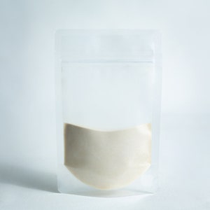 May include: A clear plastic stand-up pouch with a zip closure, filled with a light brown powder.