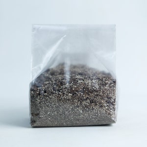 May include: A clear plastic bag filled with a dark brown and white soil-like substance.