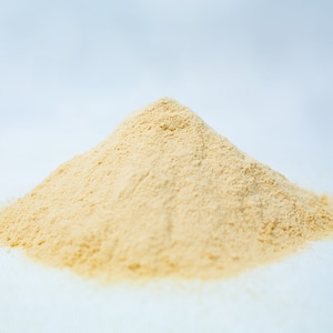 May include: A close-up of a pile of light yellow powder on a white surface.