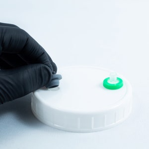 May include: A white plastic lid with two different colored stoppers. One stopper is gray and the other is green.