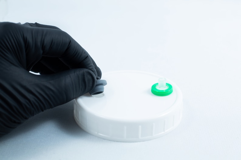 May include: A white plastic lid with two different colored stoppers. One stopper is gray and the other is green.