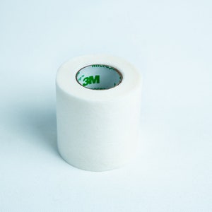 May include: A roll of white medical tape with a green 3M logo on the centre roll.