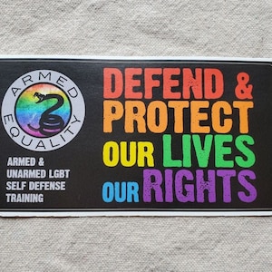May include: Black and white sticker with a rainbow colored snake logo that says "Armed Equality". The sticker also has the text "Defend & Protect Our Lives Our Rights" in rainbow colors.