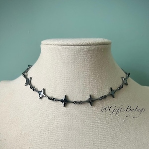 May include: A silver choker necklace with a repeating pattern of star-shaped links. The necklace is displayed on a white mannequin.