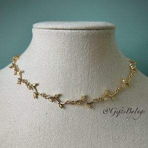 Può includere: Una collana dorata con un delicato designo a forma di vite e piccole pietre trasparenti. La collana è su un busto di manichino bianco.