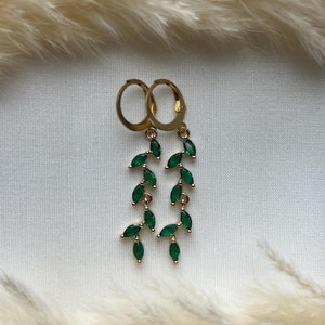 May include: Gold hoop earrings with a dangling chain of emerald green marquise-shaped stones.