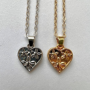 May include: Two delicate necklaces with heart-shaped pendants. The pendants are silver and gold and feature a floral design.