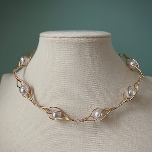 May include: A gold wire necklace with five white pearls set in a delicate, leaf-like design.