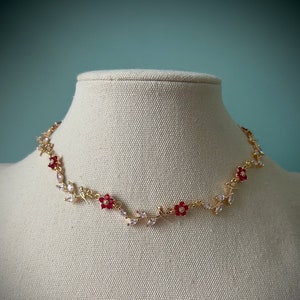 May include: A gold necklace with a delicate vine design featuring small red flowers and clear rhinestones.