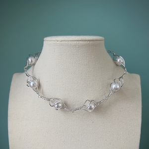 May include: A silver wire necklace with white pearls. The necklace is twisted and has a delicate design.