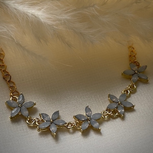May include: A gold chain necklace with five light blue flower-shaped pendants. The necklace is on a white background.