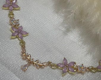 May include: A gold chain bracelet with pink flower charms and clear crystal accents. The bracelet is delicate and feminine.
