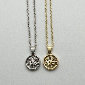 May include: Two delicate necklaces with a silver and gold pendant featuring a detailed leaf design. The pendants are round and have a raised leaf design.