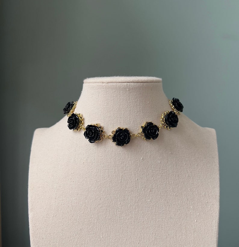 May include: A gold chain choker necklace with black rose accents. The necklace is on a white mannequin.