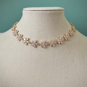 May include: A gold chain necklace with a delicate design of small, clear flower-shaped crystals.