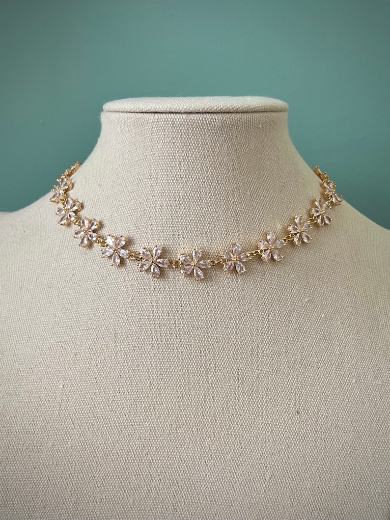 May include: A gold chain necklace with a delicate design of small, clear flower-shaped crystals.