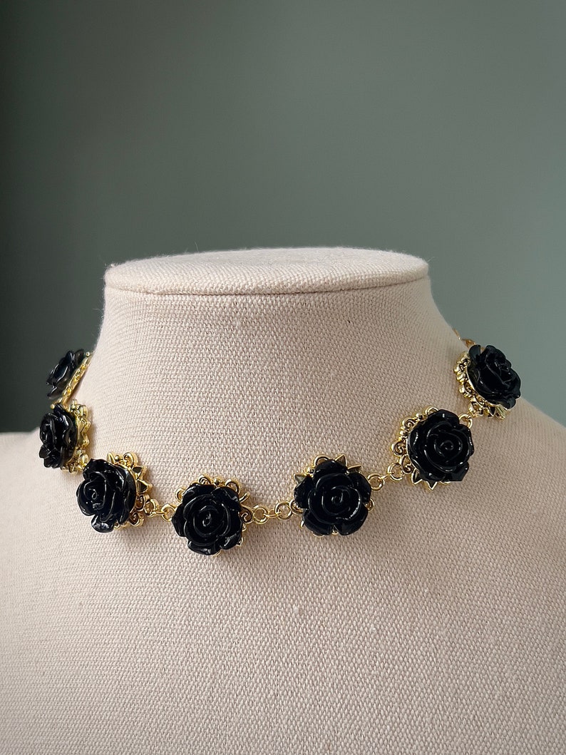 May include: A gold chain necklace with black rose-shaped charms. The necklace is on a white mannequin bust.