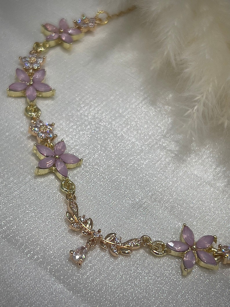 May include: A gold chain bracelet with pink flower charms and clear crystal accents.