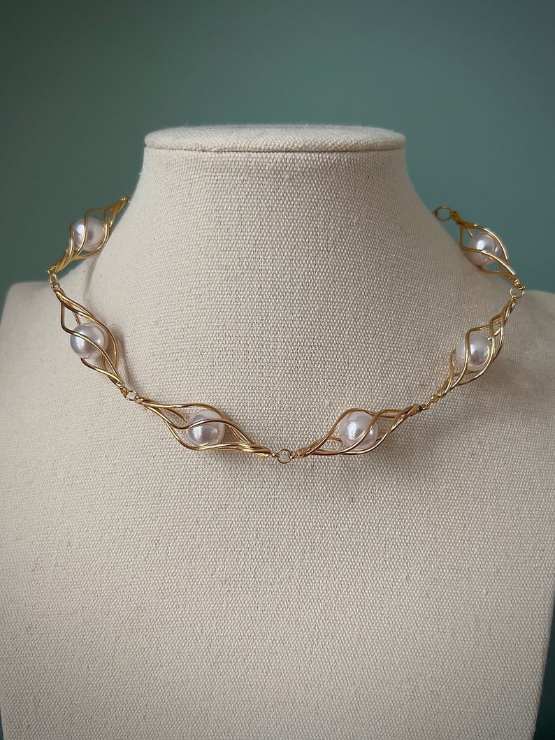 May include: A gold wire necklace with five white pearls set in a delicate, leaf-like design.
