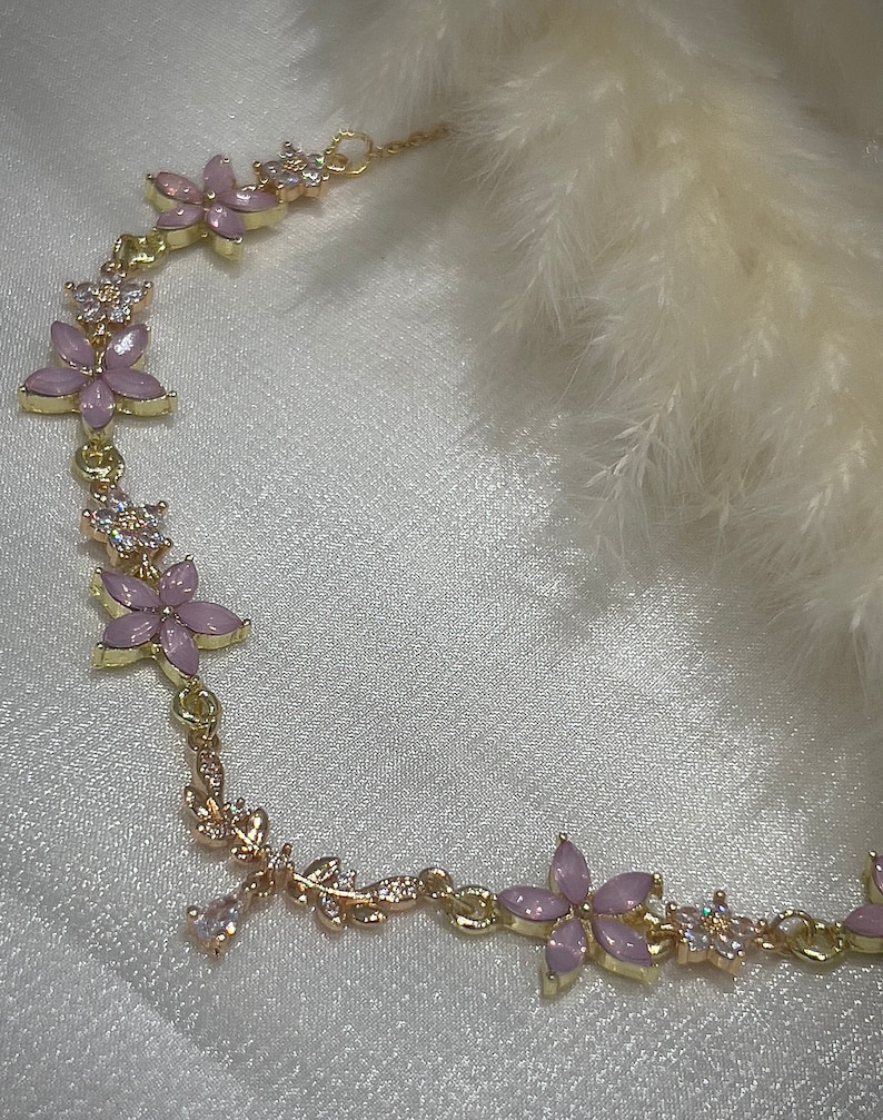 May include: A gold chain bracelet with pink flower charms and clear crystal accents. The bracelet is delicate and feminine.