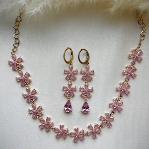 May include: A gold necklace and earrings set with pink flower-shaped charms and teardrop-shaped stones.