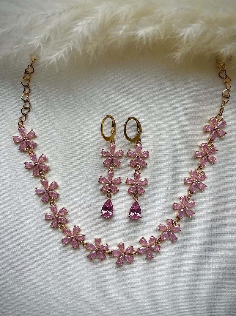 May include: A gold necklace and earrings set with pink flower-shaped charms and teardrop-shaped stones.