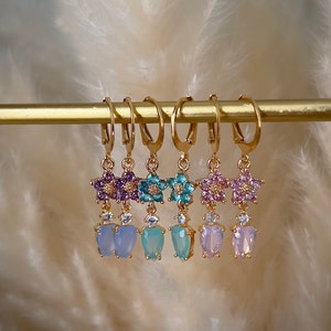 Puede incluir: Cinco pares de pendientes colgantes de oro con un dise&ntilde;o de flor y un colgante en forma de coraz&oacute;n. Las flores est&aacute;n hechas de piedras de cristal de colores y los colgantes son de vidrio opalescente.