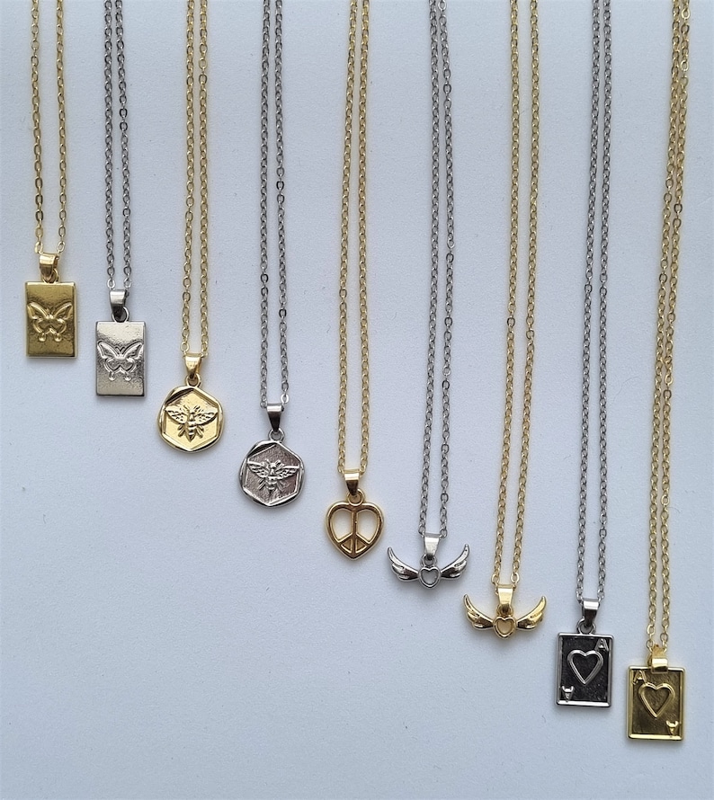 May include: A collection of necklaces with various pendant designs, including a butterfly, bee, peace sign, wings, and playing card symbols. The necklaces have either gold or silver chains and pendants, displayed against a white background.