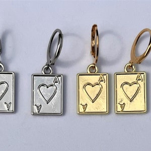 May include: Four earrings featuring a playing card design. The earrings are in silver, gunmetal, and gold tones. Each earring has a rectangular pendant with a heart and the letter "A" on it, representing the Ace of Hearts.