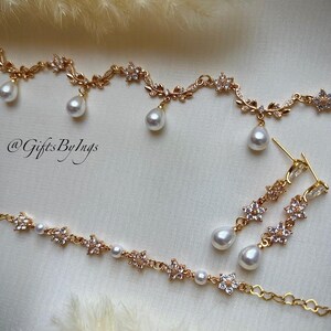 May include: A gold-toned jewelry set featuring a necklace, bracelet, and earrings. The pieces are adorned with floral and leaf designs, accented with clear crystals and dangling pear-shaped pearls. The text "@GiftsByIngs" is visible.