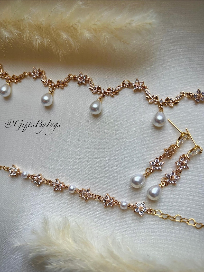 May include: A gold-toned jewelry set featuring a necklace, bracelet, and earrings. The pieces are adorned with floral and leaf designs, accented with clear crystals and dangling pear-shaped pearls. The text "@GiftsByIngs" is visible.