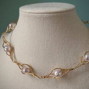 May include: A gold necklace with five white pearls set in a delicate wire cage design.