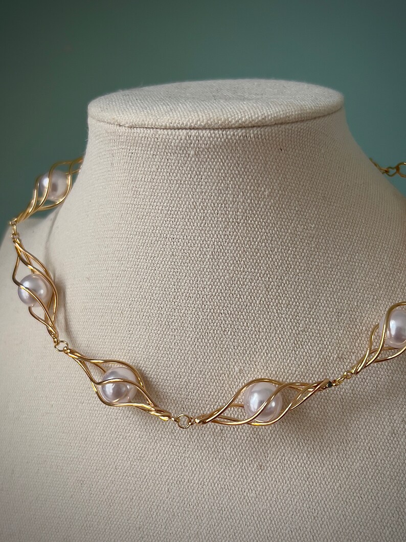 May include: A gold necklace with five white pearls set in a delicate wire cage design.