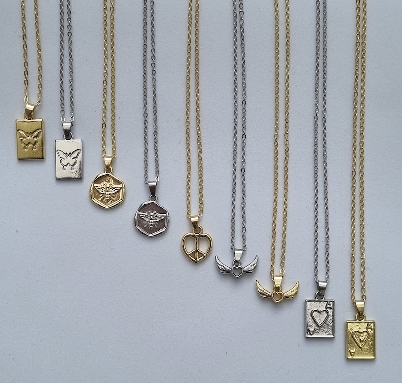 May include: A collection of delicate necklaces with various pendant designs, including butterflies, bees, peace signs, wings, and playing card symbols. The chains are silver and gold-toned, with rectangular and circular pendants.