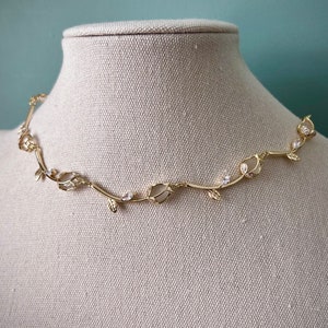 May include: A gold necklace with a delicate vine design featuring small white stones and leaves.