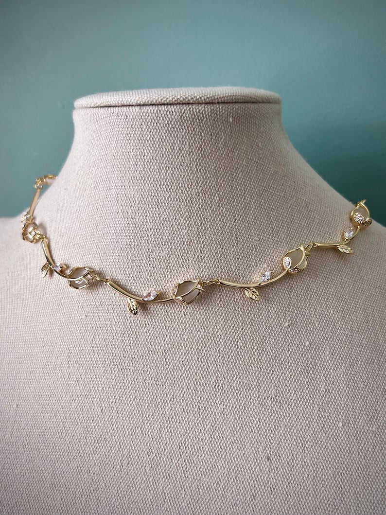 May include: A gold necklace with a delicate vine design featuring small white stones and leaves.