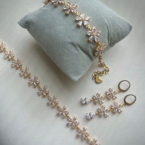 May include: A gold-tone jewelry set with a delicate flower design. The set includes a bracelet, necklace, and earrings. Each piece is adorned with clear cubic zirconia stones.