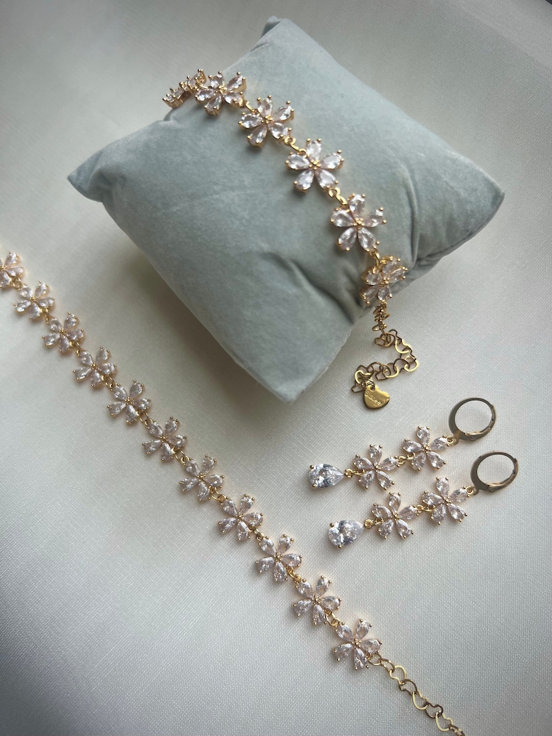 May include: A gold-tone jewelry set with a delicate flower design. The set includes a bracelet, necklace, and earrings. Each piece is adorned with clear cubic zirconia stones.