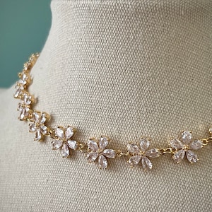 May include: A gold necklace with a delicate chain and clear crystal flower accents.
