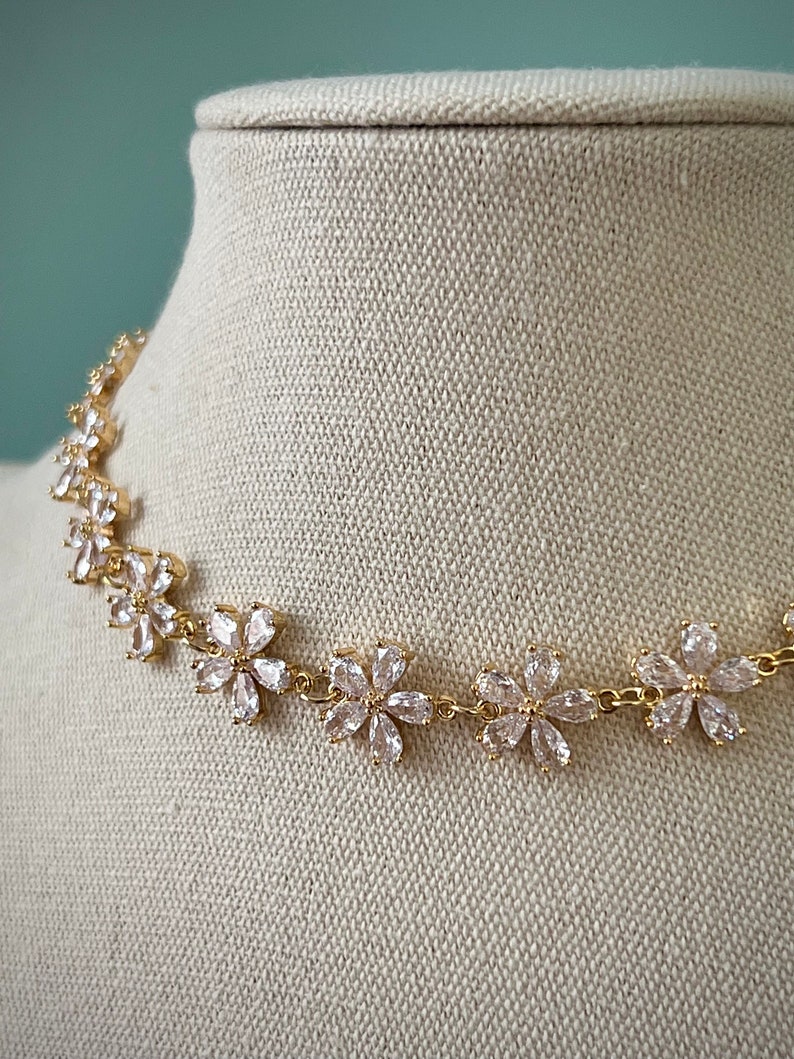 May include: A gold necklace with a delicate chain and clear crystal flower accents.