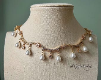 Puede incluir: Un collar dorado con un diseño delicado, con pequeños cristales transparentes y perlas colgantes en forma de lágrima. El collar se exhibe en un maniquí, mostrando sus intrincados detalles y su estilo elegante.