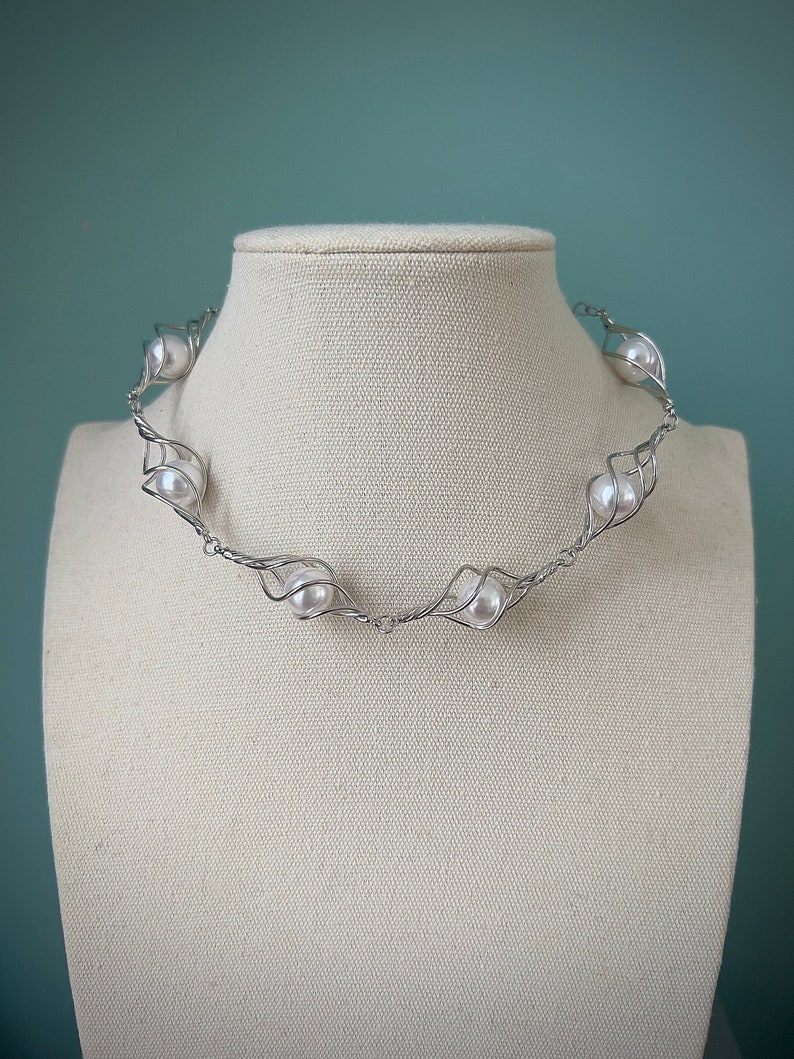 May include: A silver wire necklace with white pearls. The necklace is twisted and has a delicate design.
